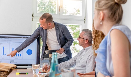 Ein Consultant präsentiert seinem Team die historischen Lizenzkosten des Auftraggebers und zeigt Lösungsmöglichkeiten zur Kostenoptimierung auf.