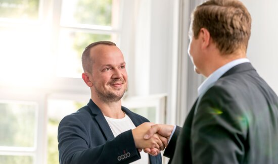 Consultant und Kunde besiegeln per Handschlag die Zusammenarbeit.